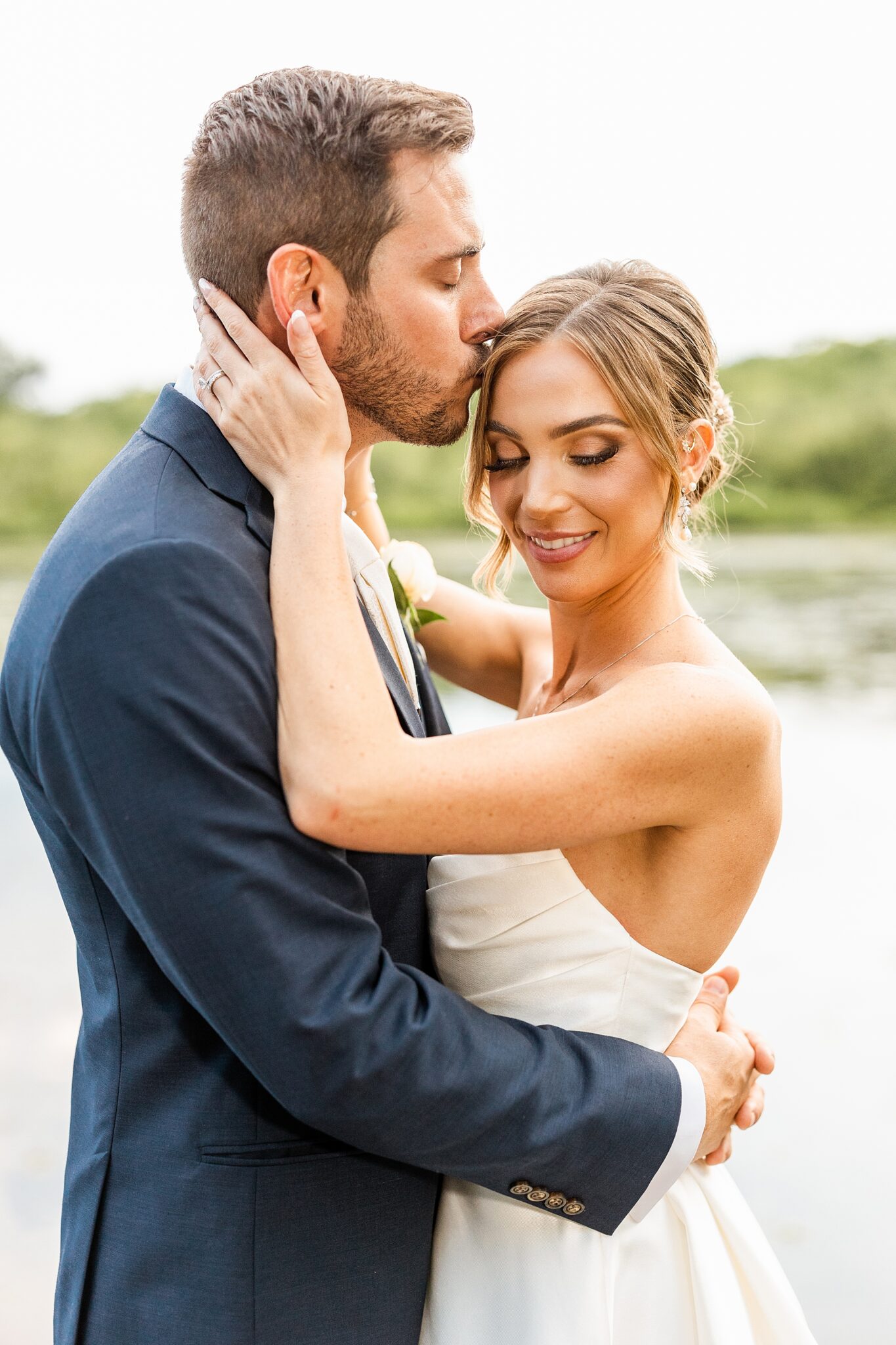 groom kisses bride's forehead on dock at the Mill Lakeside Manor